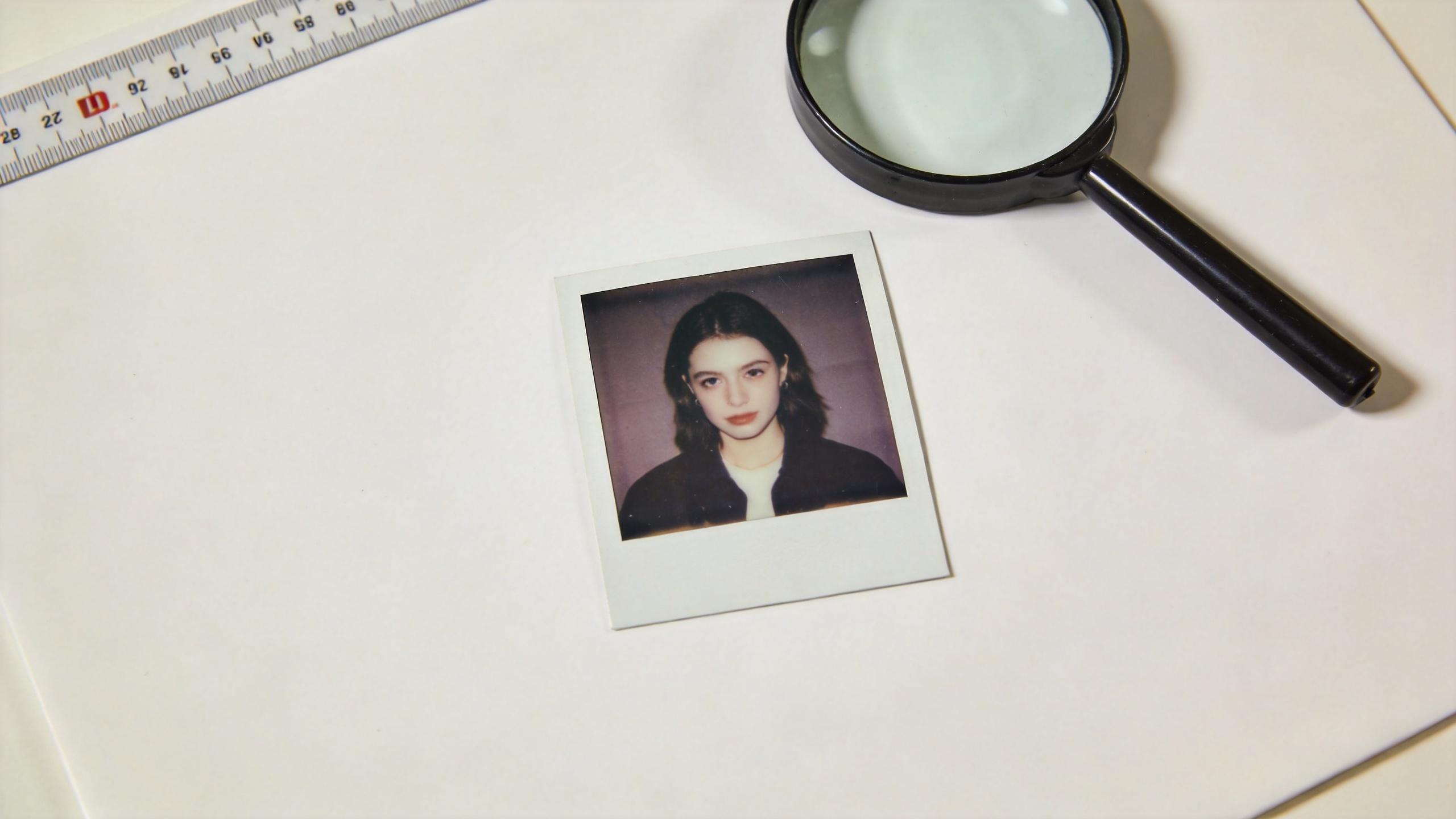 Polaroid portrait on a white desk with a magnifying glass and ruler