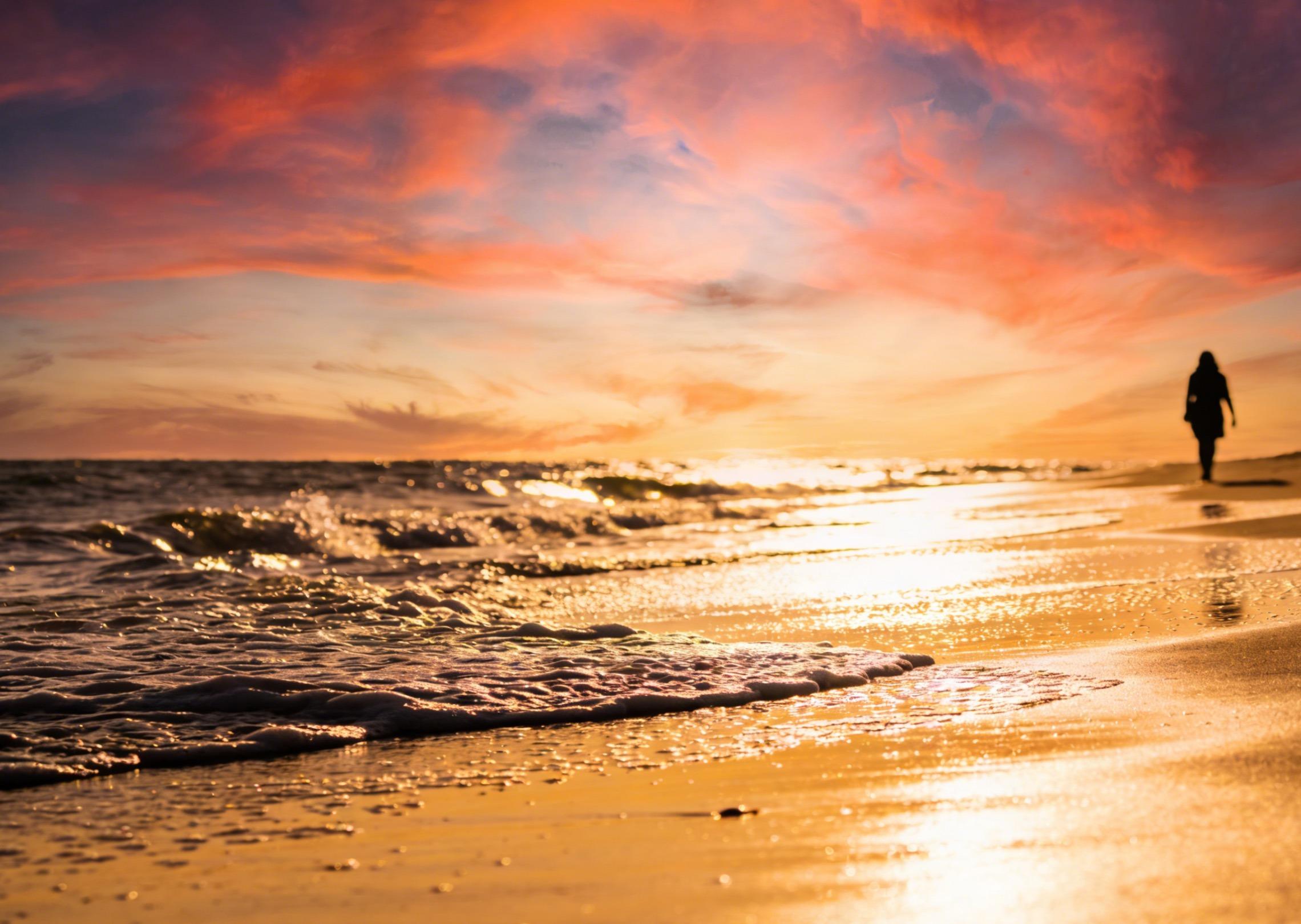 Erstellen Sie ein Video von einem Strand bei Sonnenuntergang mit sanft rollenden Wellen und einer Person, die am Ufer entlang läuft