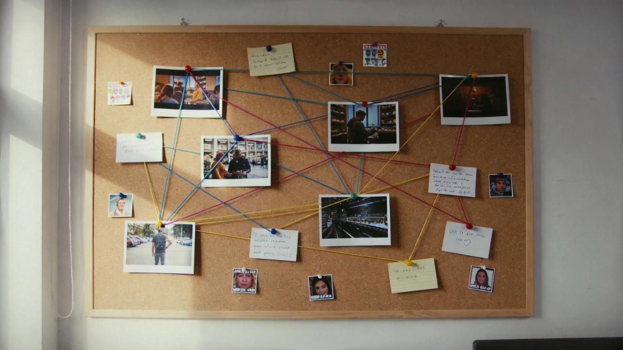 Corkboard covered with pinned photos, notes, and colored string connections