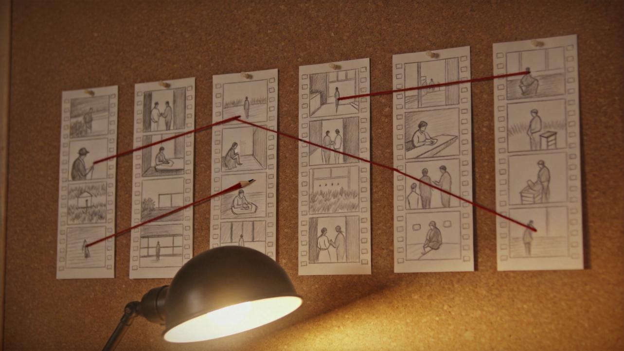 Storyboard sketches pinned to a corkboard, linked by red strings above a desk lamp.